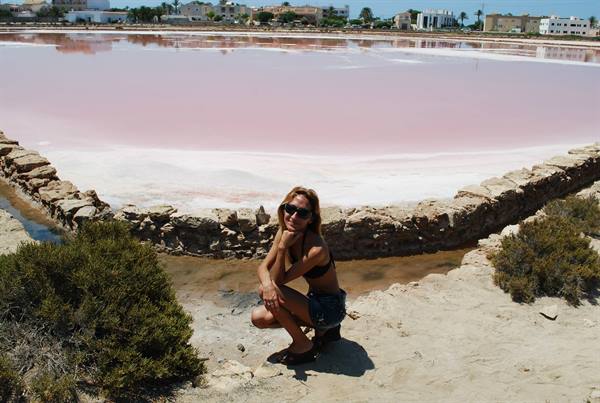 Woman crouching beside the pink salt flats of San Pedro del Pinatar, dry stone walls