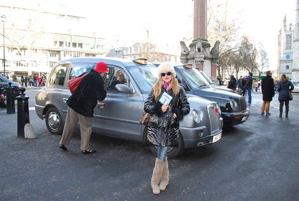 Woman in white hat posing beside London black cabs near Westminster