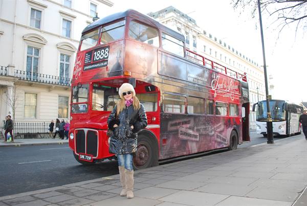 Woman in white hat and black coat in front of a red double-decker bus in London