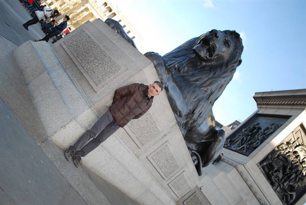 Man poses beside the bronze lion on Nelson's base at Trafalgar Square