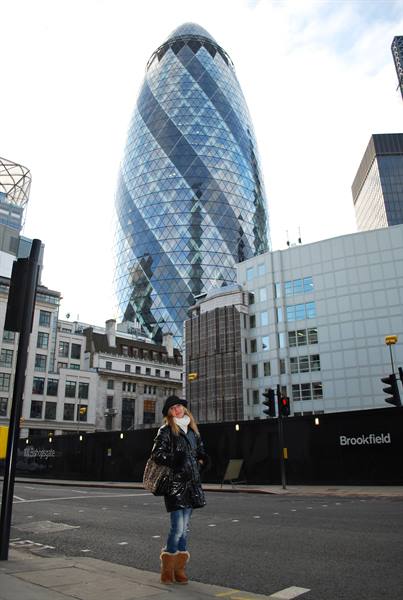 Woman in black coat crosses the street in front of the Gherkin skyscraper, London