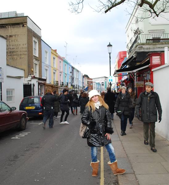 Girl in black coat posing on street among colorful houses of Portobello Road