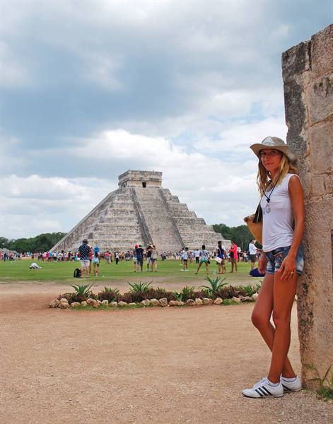 Tourist in hat leaning on stone wall in front of Chichén Itzá pyramid