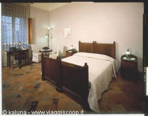 Hotel room with dark wooden double bed, natural light from window, terracotta floor