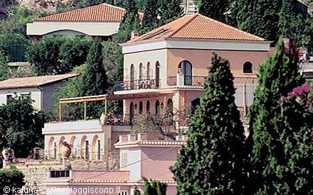 Pink villa with tiled roof among pines and cypresses on sunny Mediterranean hillside