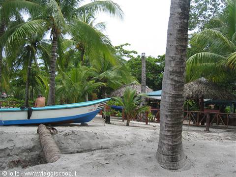 Blue and white fishing boat on the sand among palms and thatched huts