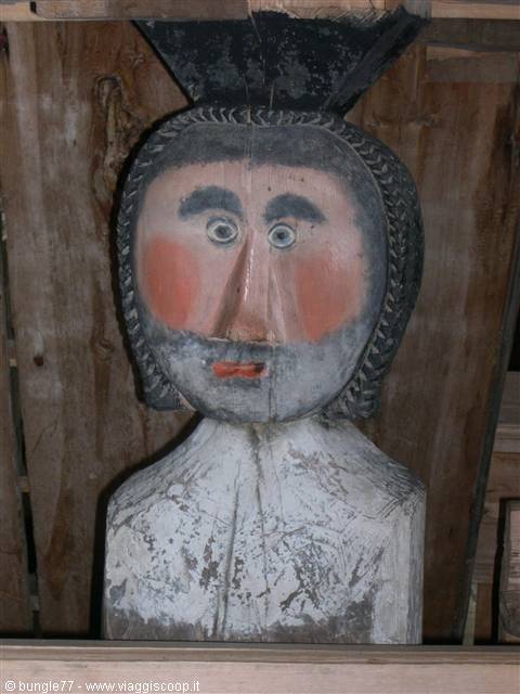 Carved painted wooden figure with colored face, sheltered inside a hut