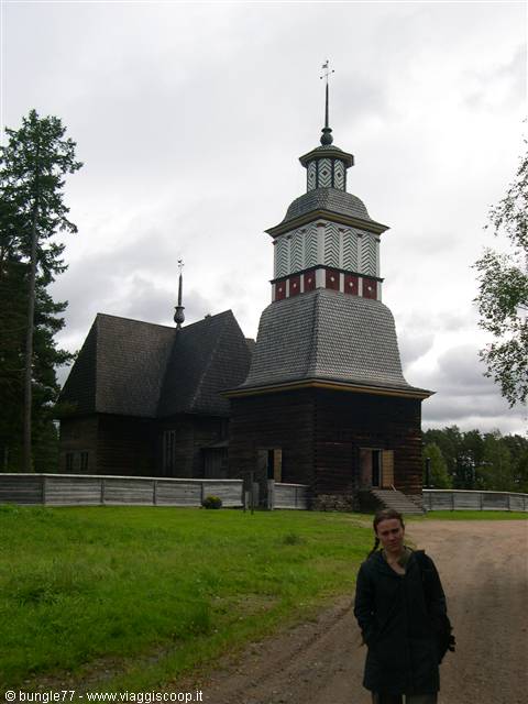 Traveler in front of the old log church of Petäjävesi under gray sky