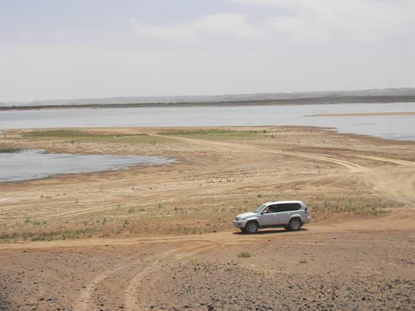 White SUV on sandy track, lake and arid shores in the background
