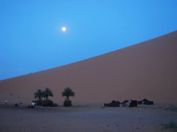 Full moon above the giant sand dune, palm trees and nomad tents