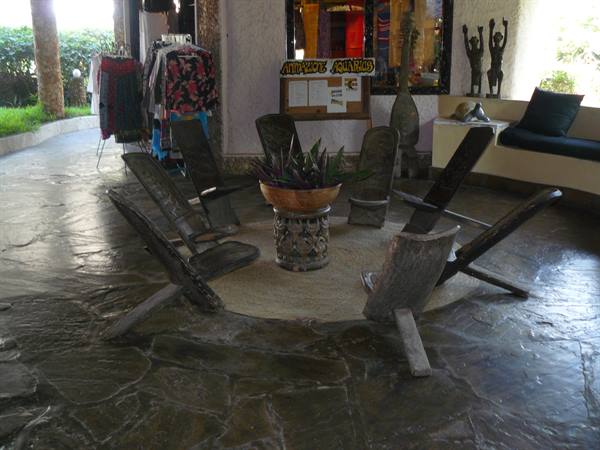 Carved wooden chairs around a plant pot on stone floor, hotel lobby