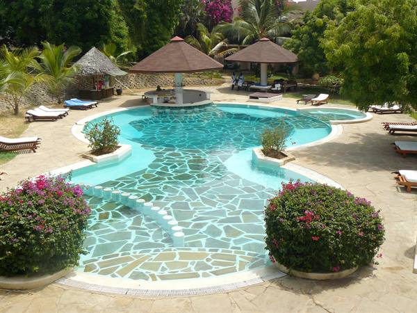Stone-bottomed pool with thatched umbrellas, sun loungers and blooming bougainvillea