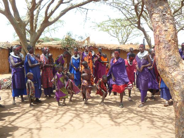 Maasai women and children in purple robes dancing under village trees