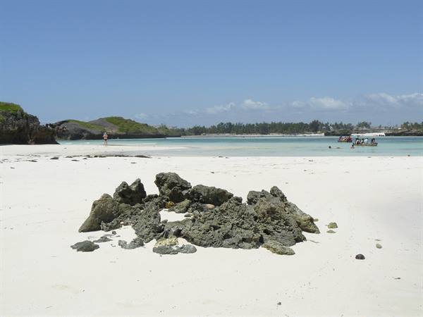 Coral rocks on white sand, boats and swimmers in Watamu's turquoise water