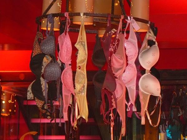 Colorful bras hanging from a metal wheel under red shop lights