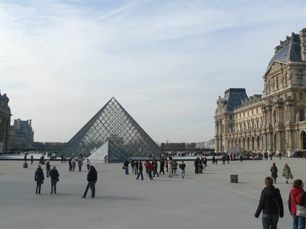 Tourists walk across the Louvre courtyard beside the great glass pyramid