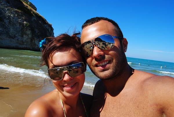 Couple in sunglasses taking selfie on beach beneath rocky cliff