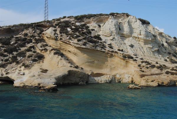 White and ochre limestone cliff above turquoise water, antennas on top