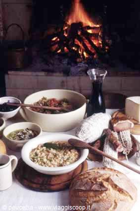 Table set with bread, salami, soup and wine before a lit fireplace