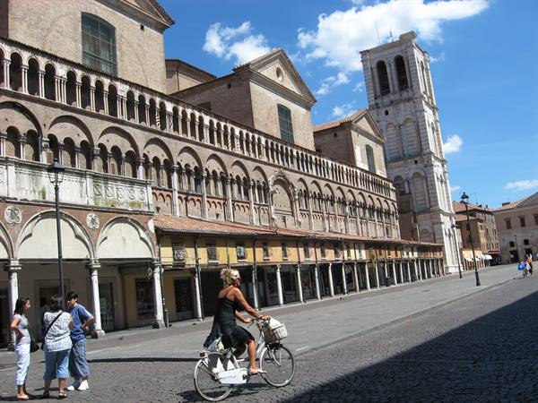Woman cycling past Ferrara cathedral with its marble bell tower