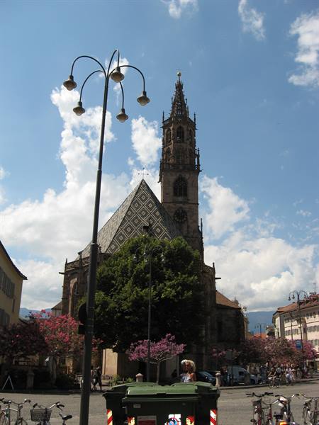 Gothic bell tower of Bolzano Cathedral among blooming trees and bicycles