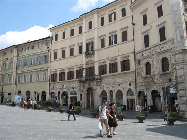 Tourists walking across Piazza del Comune in Assisi among historic arcaded buildings