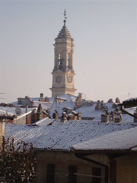 Clock bell tower above snow-covered tiled rooftops in winter light