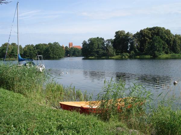 Red rowboat among reeds, moored sailboat, brick cathedral across the lake