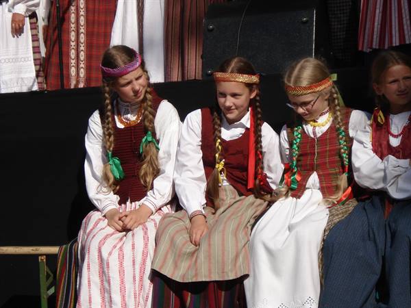 Blonde girls with braids and traditional linen folk costumes sitting in the shade