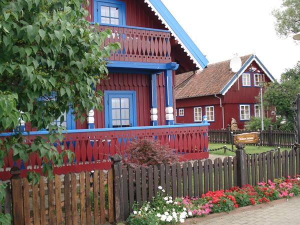 Red wooden houses with blue trim, wooden fences and colorful flowers along the road