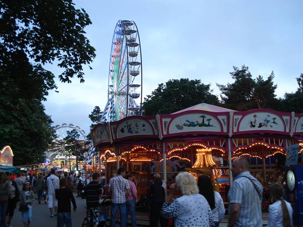 Illuminated carousel and Ferris wheel among crowds at an evening funfair