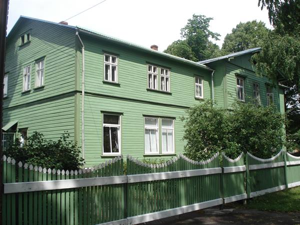 Green wooden house with painted picket fence, cloudy day among trees