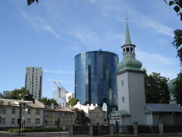 White wooden church tower with green spire beside a glass skyscraper, Tallinn