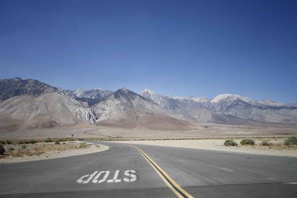 Paved road with painted stop marking pointing toward snowy rocky mountains under blue sky