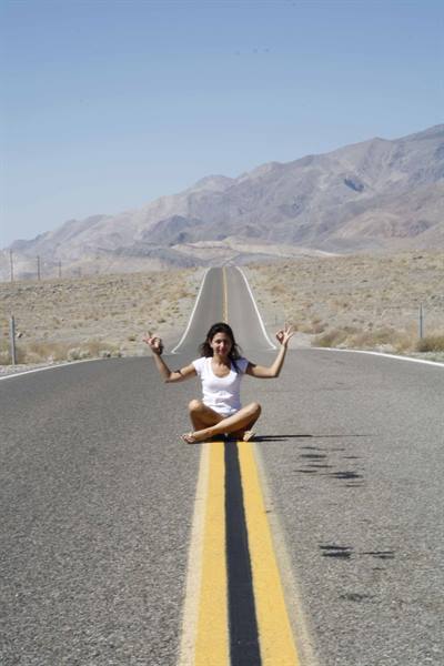 Woman sitting on double yellow line of empty desert road by arid mountains