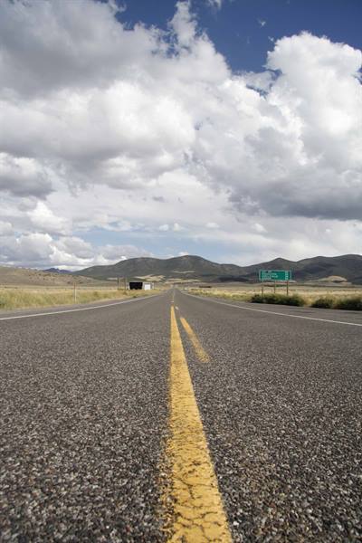 Asphalt highway with yellow centerline, green road sign and hills under clouds