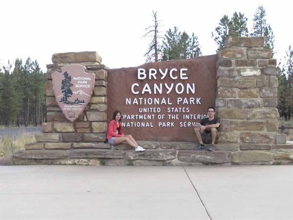 Two tourists sitting on the stone wall at Bryce Canyon National Park entrance
