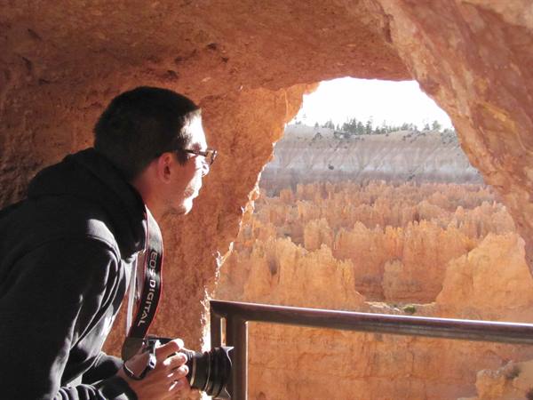 Tourist with camera gazes at Bryce Canyon orange hoodoos from a cave
