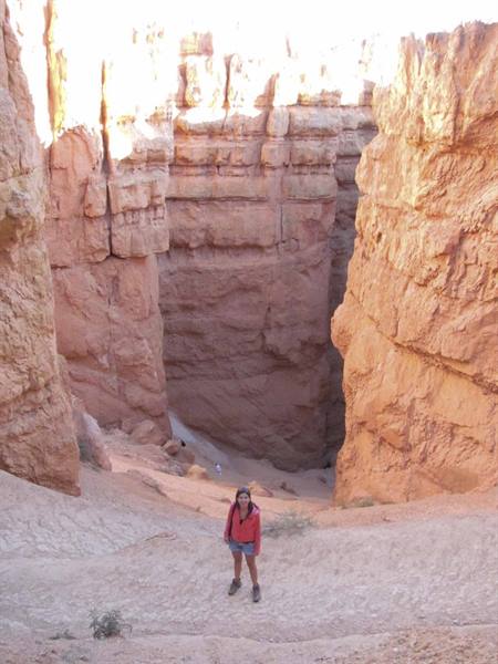 Hiker in red jacket on sandy trail among Bryce Canyon orange rock spires