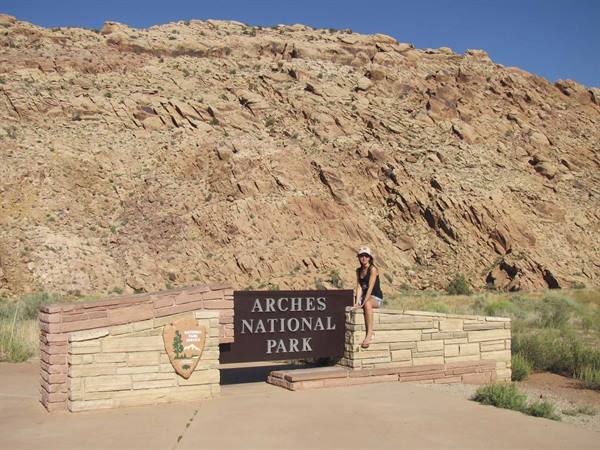 Woman sitting on the stone wall at Arches National Park entrance