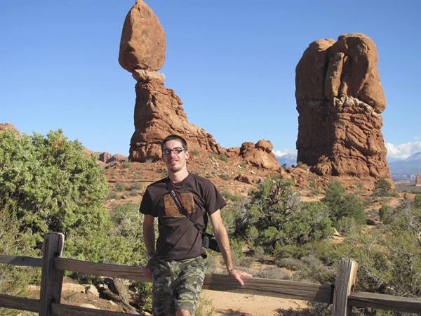 Tourist leaning on wooden fence in front of Balanced Rock at Arches