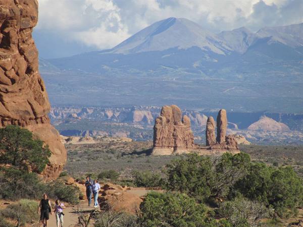 Hikers walk the sandy trail among red rock formations at Arches