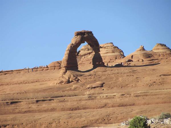 Red sandstone arch under blue sky, tourists standing on the rock