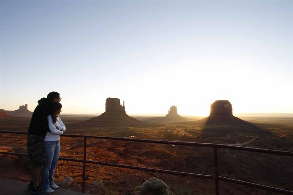 Couple embracing at wooden railing admiring Monument Valley's red buttes at sunrise