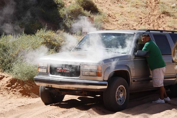 Gray GMC SUV with overheated engine, white steam, smiling man in green shirt