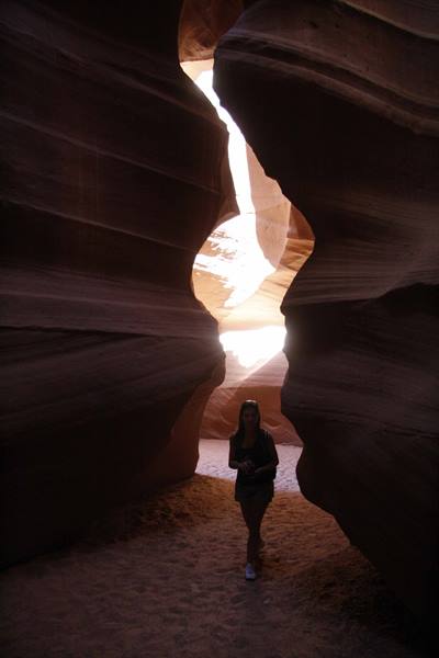 Woman walks on sand between glowing sandstone walls of Antelope Canyon