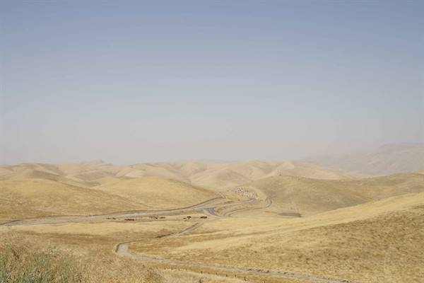 Dry yellowish hills with winding road and trucks, hazy sky