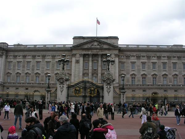 Crowds of tourists in front of Buckingham Palace gates under cloudy sky