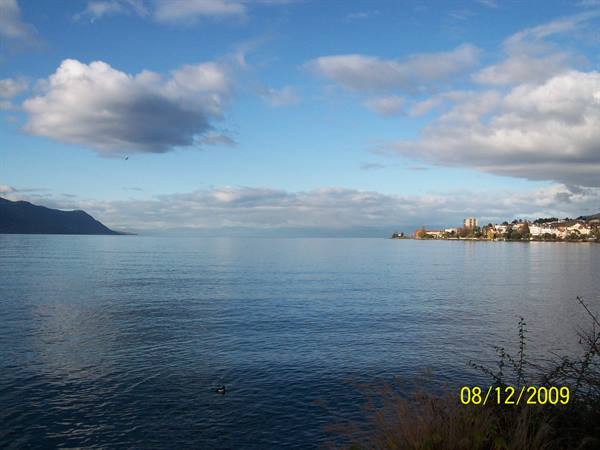 Calm lake with mountain on the left, town along the right shore under clouds
