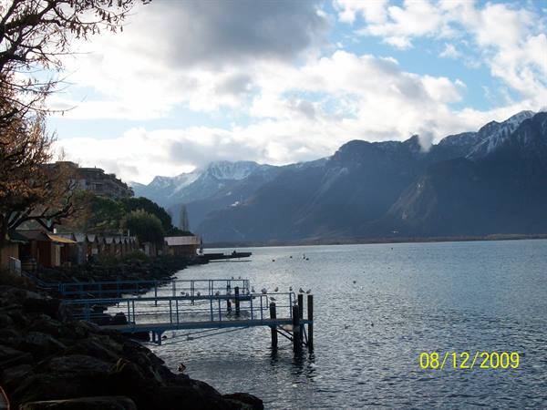 Metal pier on the lake, seagulls, snowy mountains, villas along the shore